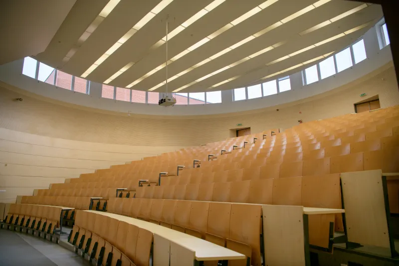 Tiered wooden seating in the Audmax lecture hall of Óbuda University under a curved skylight ceiling