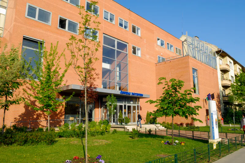 Red-brick and glass facade of Óbuda University's main building on Bécsi út, with the blue Óbudai Egyetem sign above the entrance